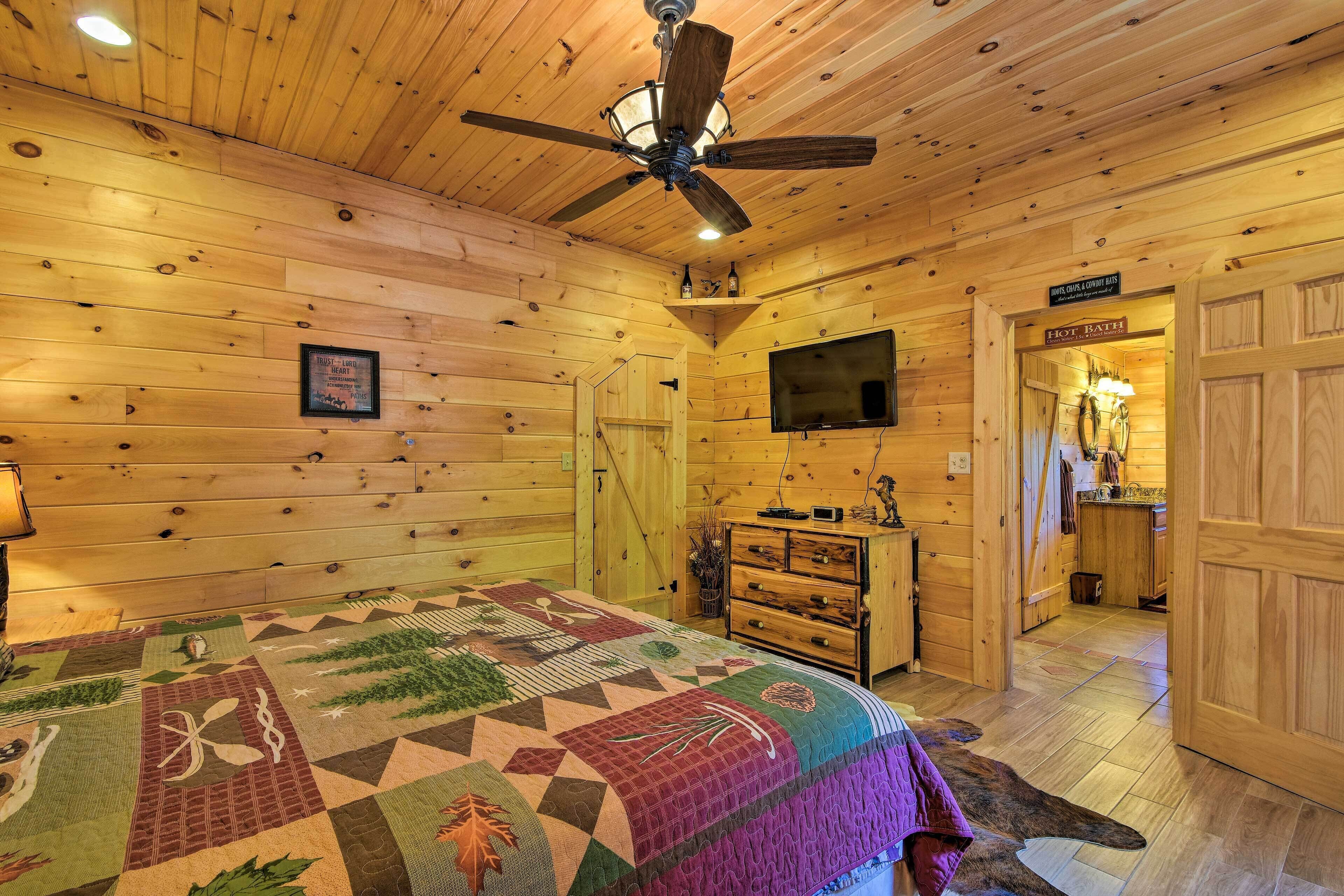 A wooden cabin interior with a bed, a ceiling fan, a television, and a sign for the hot tub.