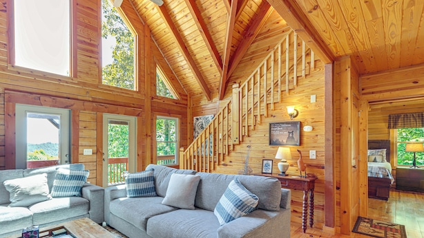 Ein gemütliches Blockhäuschen-Interieur mit einer Holztreppe, einer Couch mit Karo-Kissen und einem Essbereich.