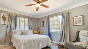 Une chambre à coucher avec un grand lit, une chaise, une table de chevet et un ventilateur de plafond.