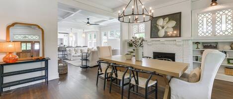 A spacious dining area with a wooden table and black chairs, a chandelier, and a white fireplace.