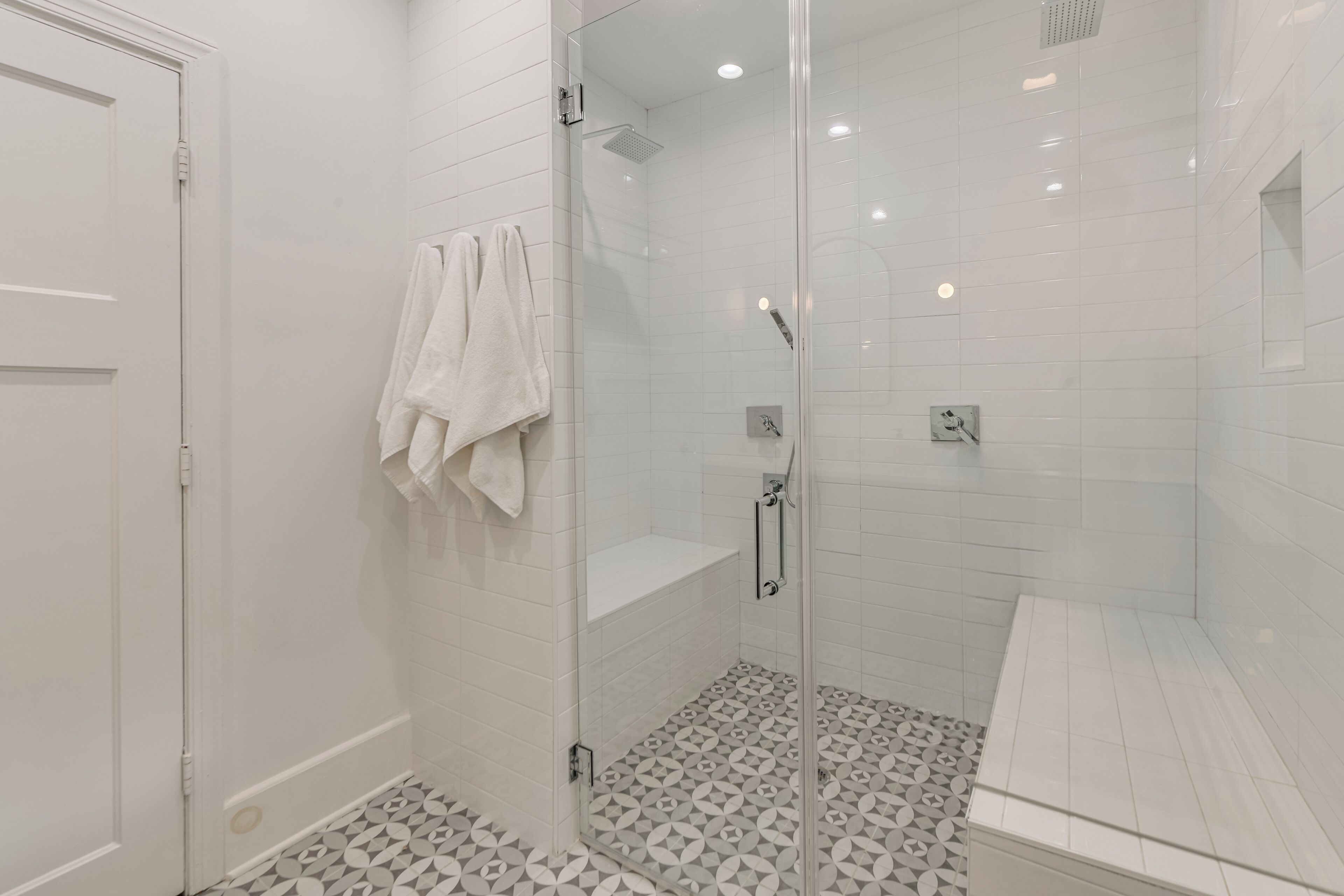 Un bagno moderno con pareti piastrellate di bianco, un box doccia in vetro, una panca e un porta asciugamani.