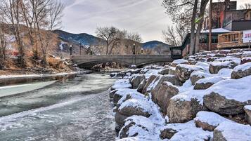 A stone bridge over a partially frozen river, with snow-covered rocks and bare trees in the background.