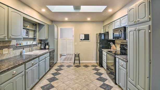 A kitchen with grey cabinets, a black refrigerator, a microwave, and a stove. There is a window above the sink and a small stool in the center. - 0651: Central Salida Home 5 Blocks to Dtwn & River (Salida)