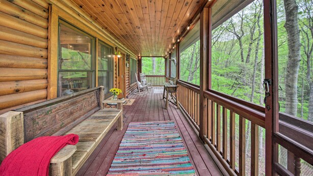 Una cabaña de madera con porche cubierto, ventanas amplias y vistas a un bosque.