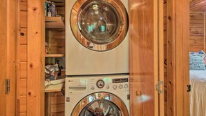 A stacked washer and dryer unit in a wooden cabin with a visible shelf above the dryer. - Peaceful Blue Ridge Cabin w/ Decks & Fire Pit (Blue Ridge)