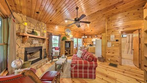 Un interior de cabaña acogedor con chimenea, pisos de madera, un sofá de cuadros y una zona de comedor.