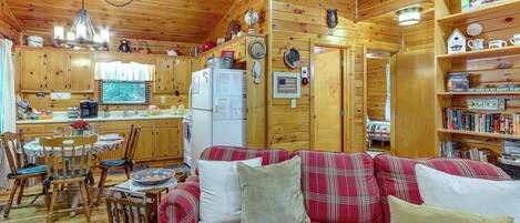 A cabin interior with a dining area, kitchen, and a cozy living space with a plaid sofa.