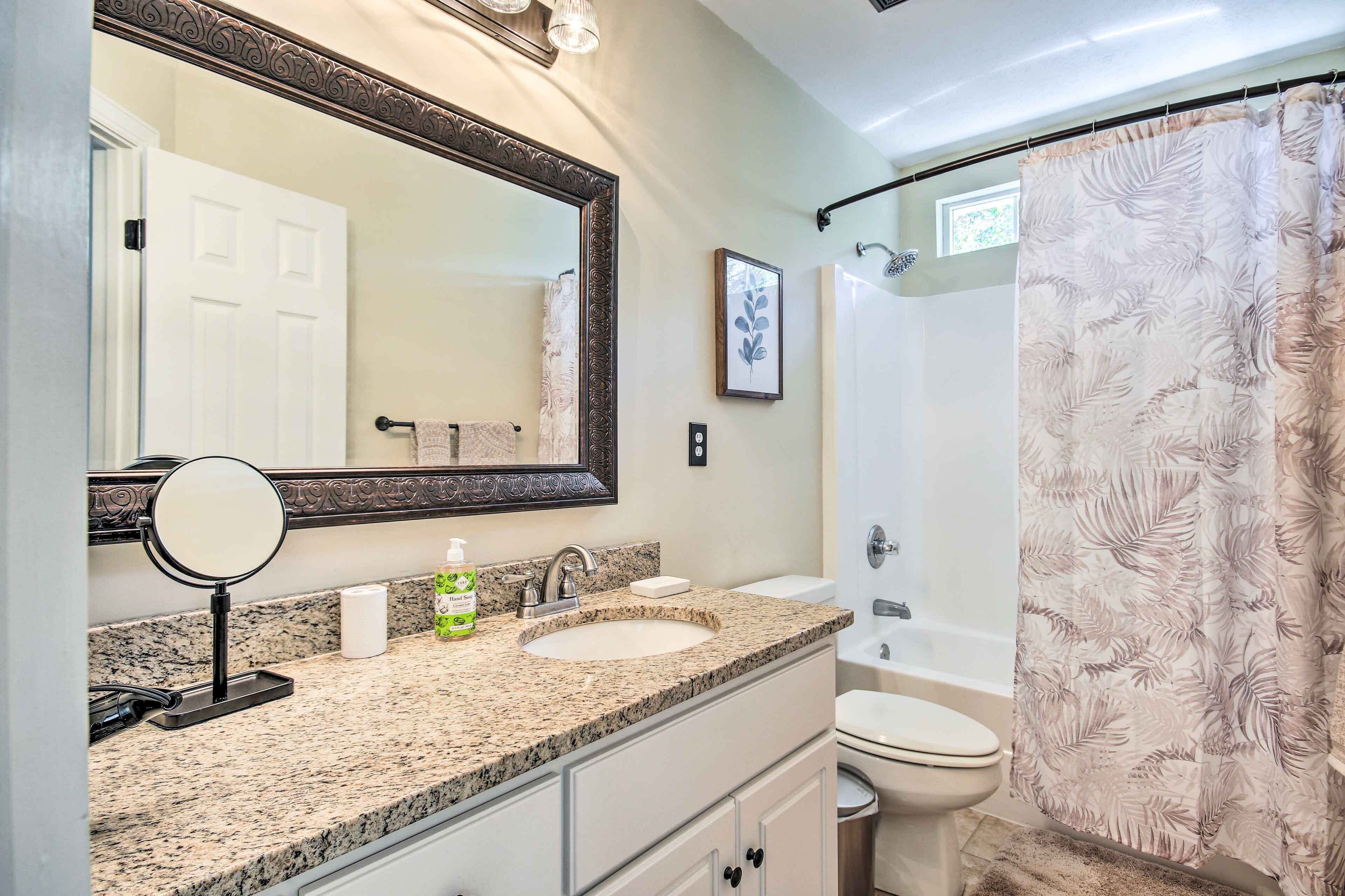 A bathroom with a granite countertop, a sink, a mirror, a toilet, and a shower with a leaf-patterned curtain.