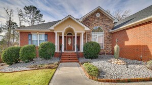 A two-story brick house with a front porch, a central entrance, and a small garden area with gravel and shrubs. - Gorgeous Evans Retreat < 14 Mi to Augusta! (Evans)