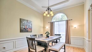 A dining room with a wooden table, chairs, and a bench. There is a chandelier, a painting on the wall, and a window with curtains. - Gorgeous Evans Retreat < 14 Mi to Augusta! (Evans)