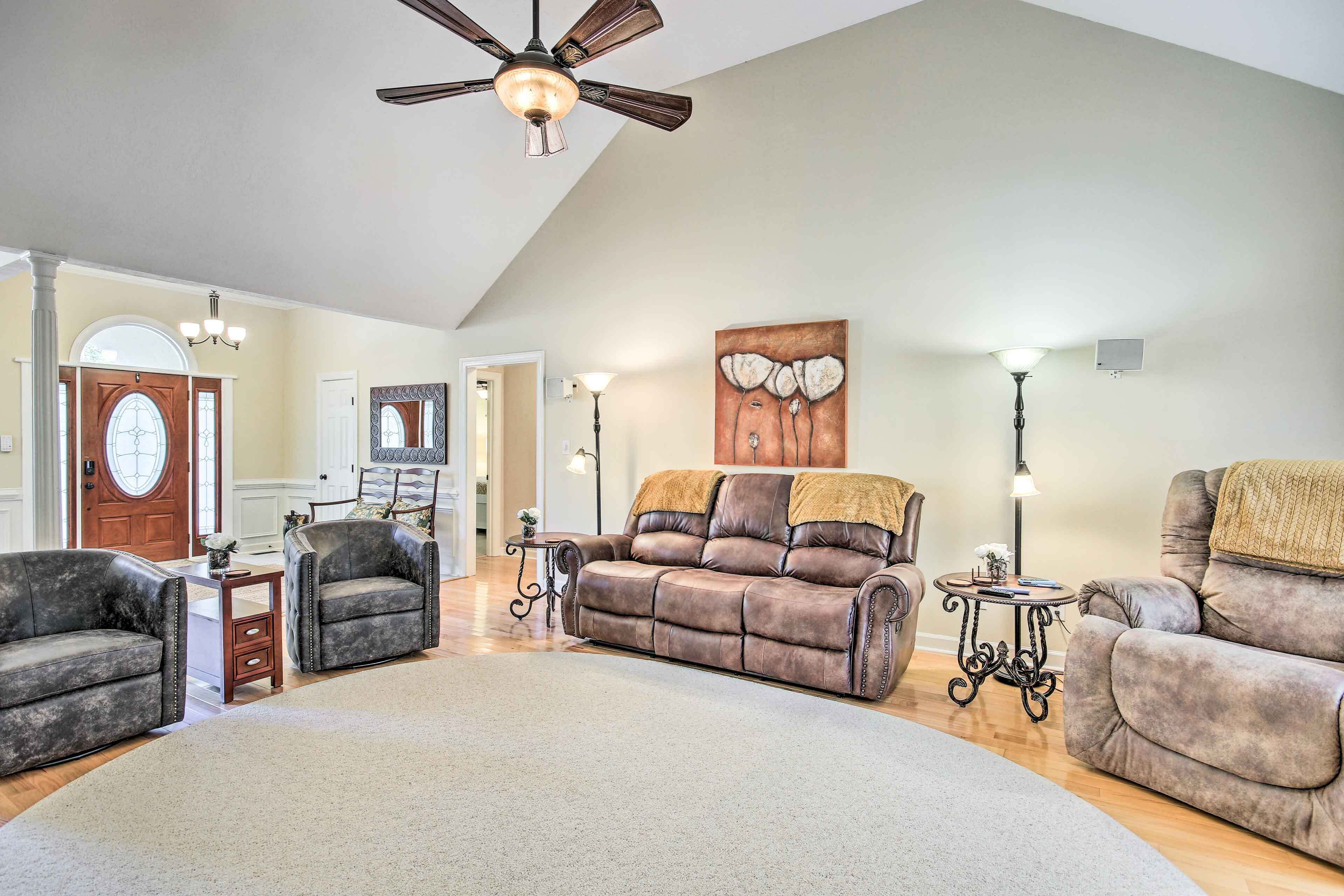 A spacious living room with a large brown leather sofa, two armchairs, a coffee table, and a ceiling fan.
