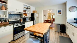 Una cocina moderna con armarios blancos, una isla de madera, electrodomésticos de acero inoxidable y un comedor con candelabro.