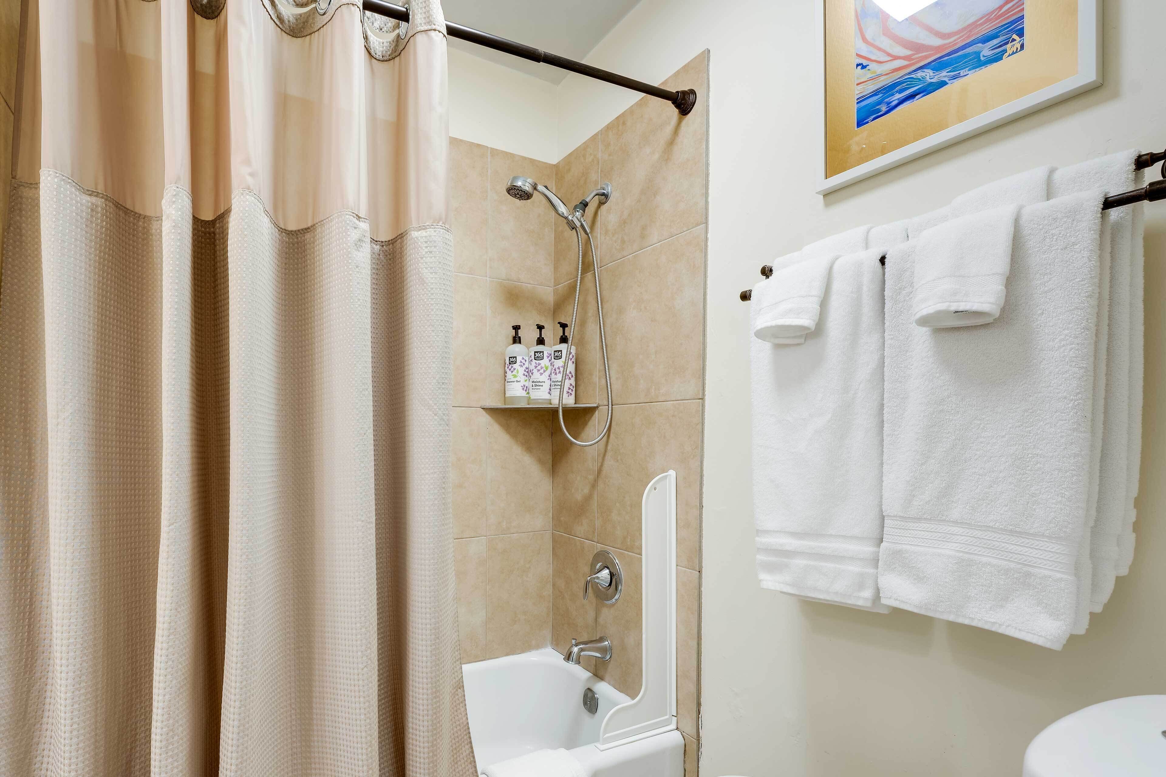 A bathroom with a shower, a sink, and two towels hanging on a rack.
