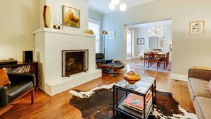 Una sala de estar con chimenea de ladrillo blanco, un sofá de cuero, una mesa de centro de vidrio y un tapete de cuero de vaca.