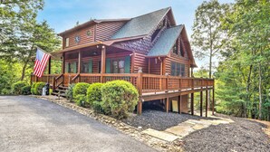 A log cabin with a deck, surrounded by trees and a flag. - Serene Blue Ridge Cabin ~ 3 Mi to Downtown! (Blue Ridge)