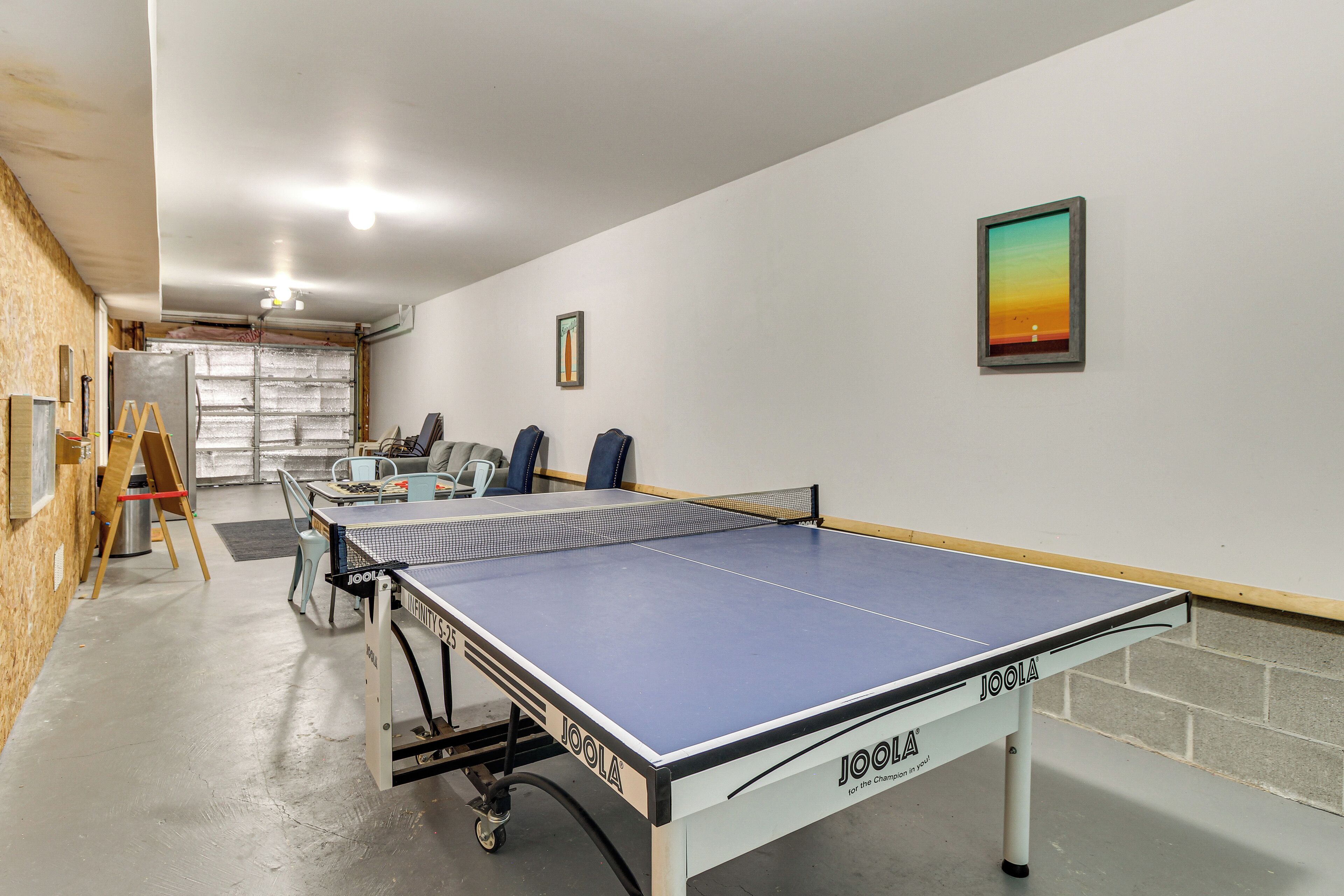 Una mesa de ping pong en una habitación con pared blanca y un cuadro enmarcado.