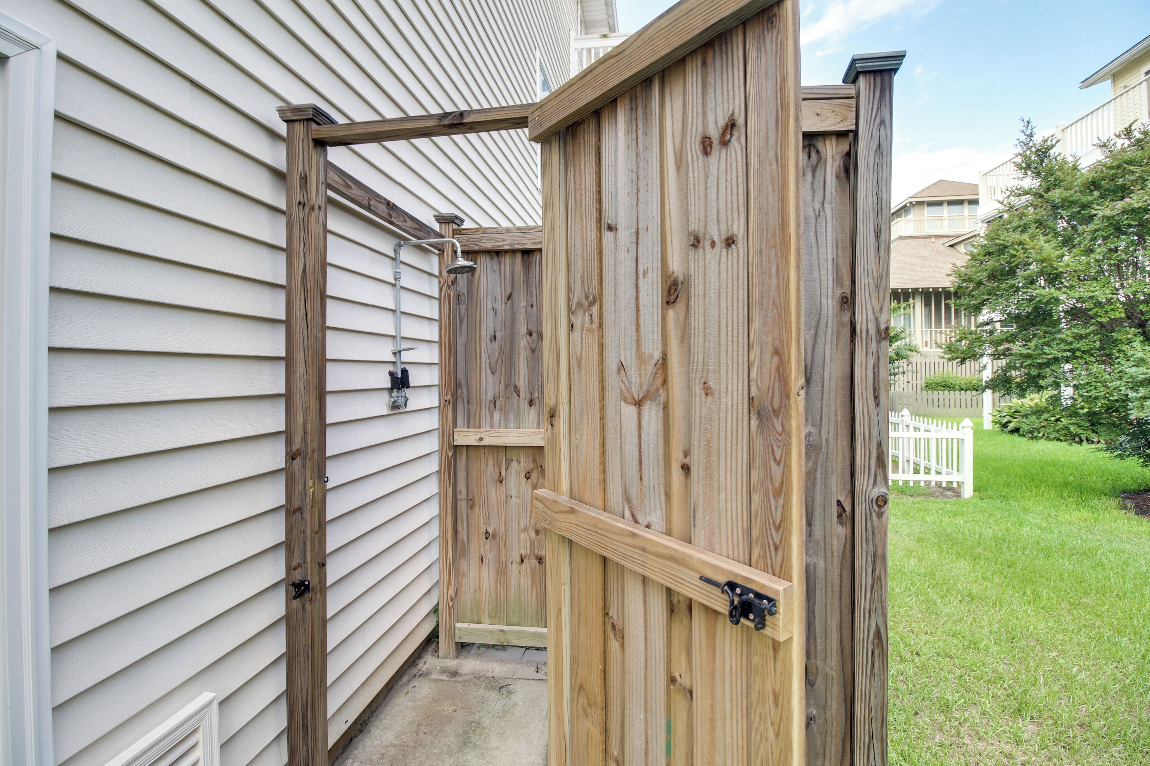 A wooden gate leading to a backyard with a white fence and a tree.