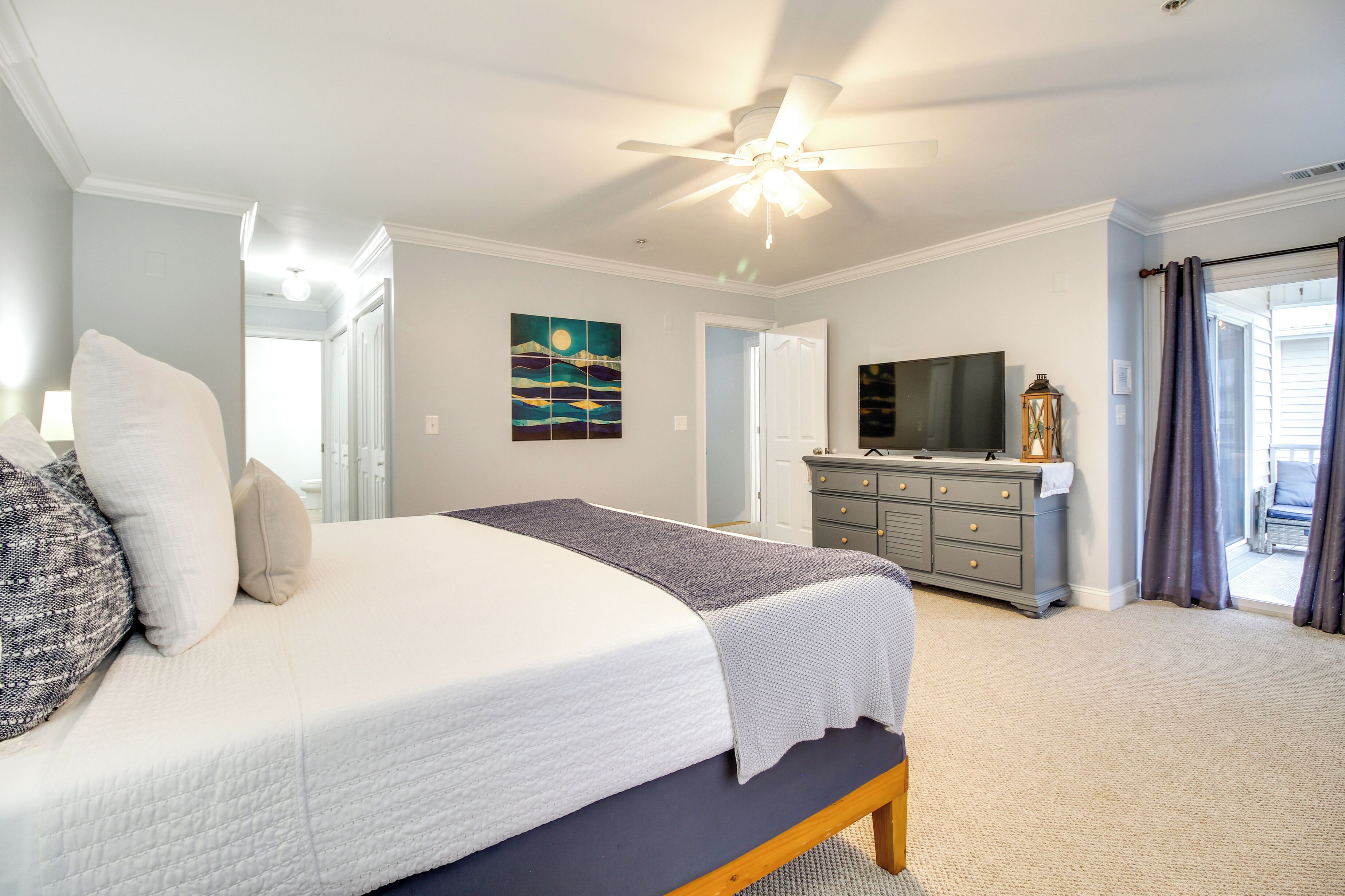 Une chambre à coucher comprenant un lit, une commode, un téléviseur et un ventilateur de plafond.