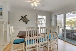 A dining area with a wooden table and white chairs, a ceiling fan, and a view through a glass door.