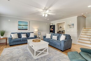 A living room with two blue sofas, a white coffee table, and a ceiling fan.