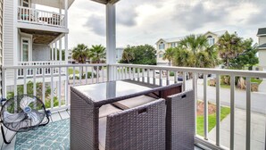 A balcony with wicker furniture, a fan, and a view of neighboring houses and palm trees.
