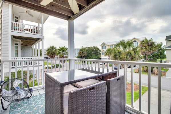 A balcony with wicker furniture, a fan, and a view of neighboring houses and palm trees.