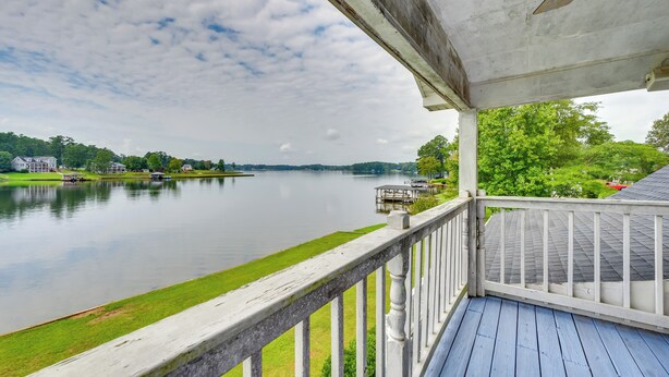 A waterfront view from a covered deck with a railing, overlooking a calm lake and distant buildings.