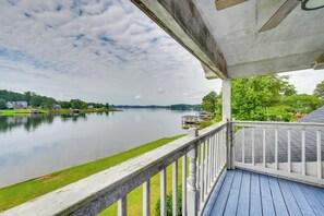 A waterfront view from a covered deck with a railing, overlooking a calm lake and distant buildings. - Waterfront Sparta Retreat w/ Dock, Deck & Grill (Milledgeville)