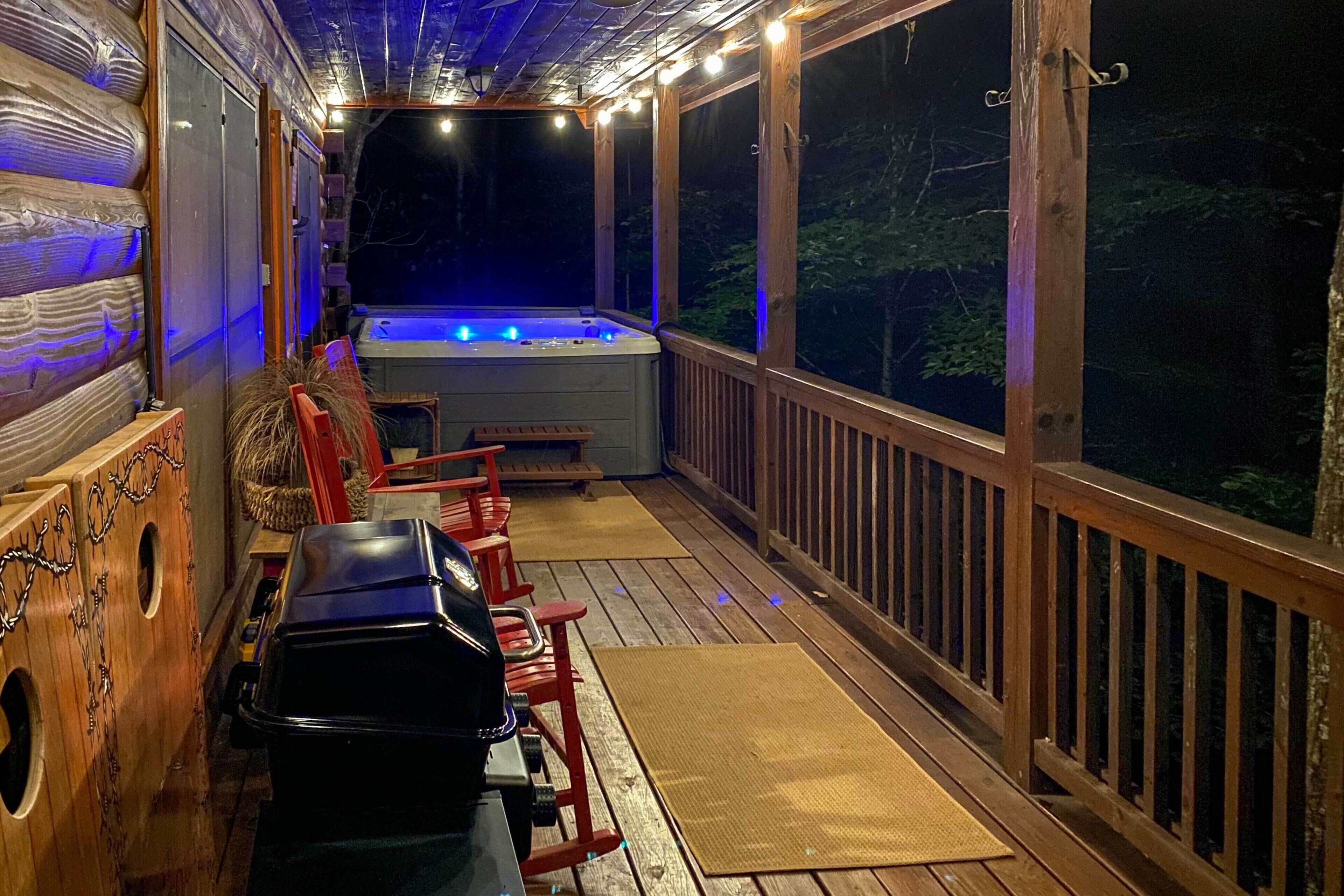 Een houten terras met een jacuzzi, barbecue en zithoek.