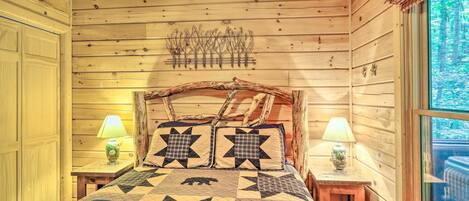 A wooden cabin bedroom with a bed, two nightstands, a window, and a wall-mounted light fixture.