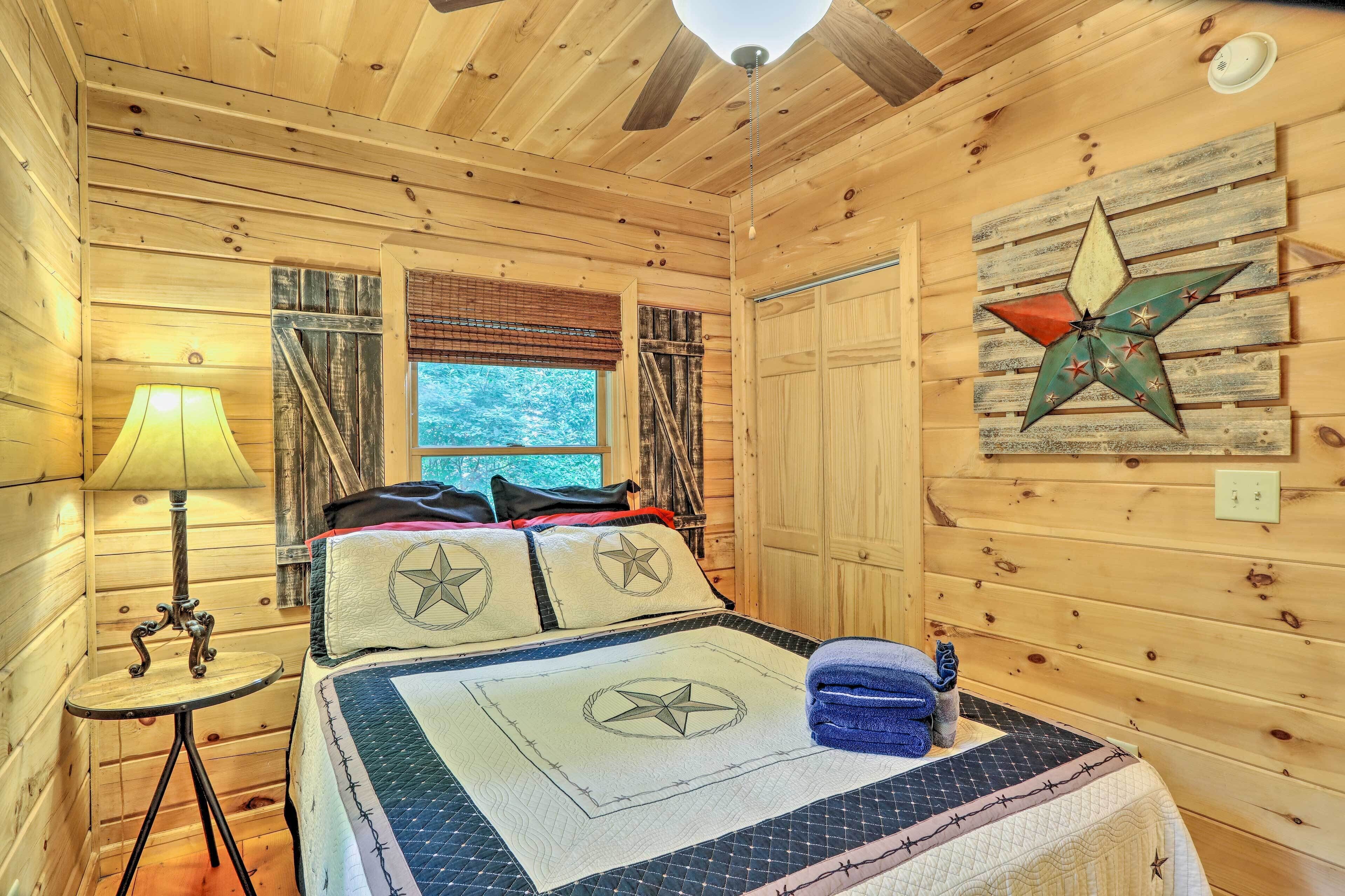 A wooden cabin room with a bed, a lamp, a star decoration, and a window with blinds.