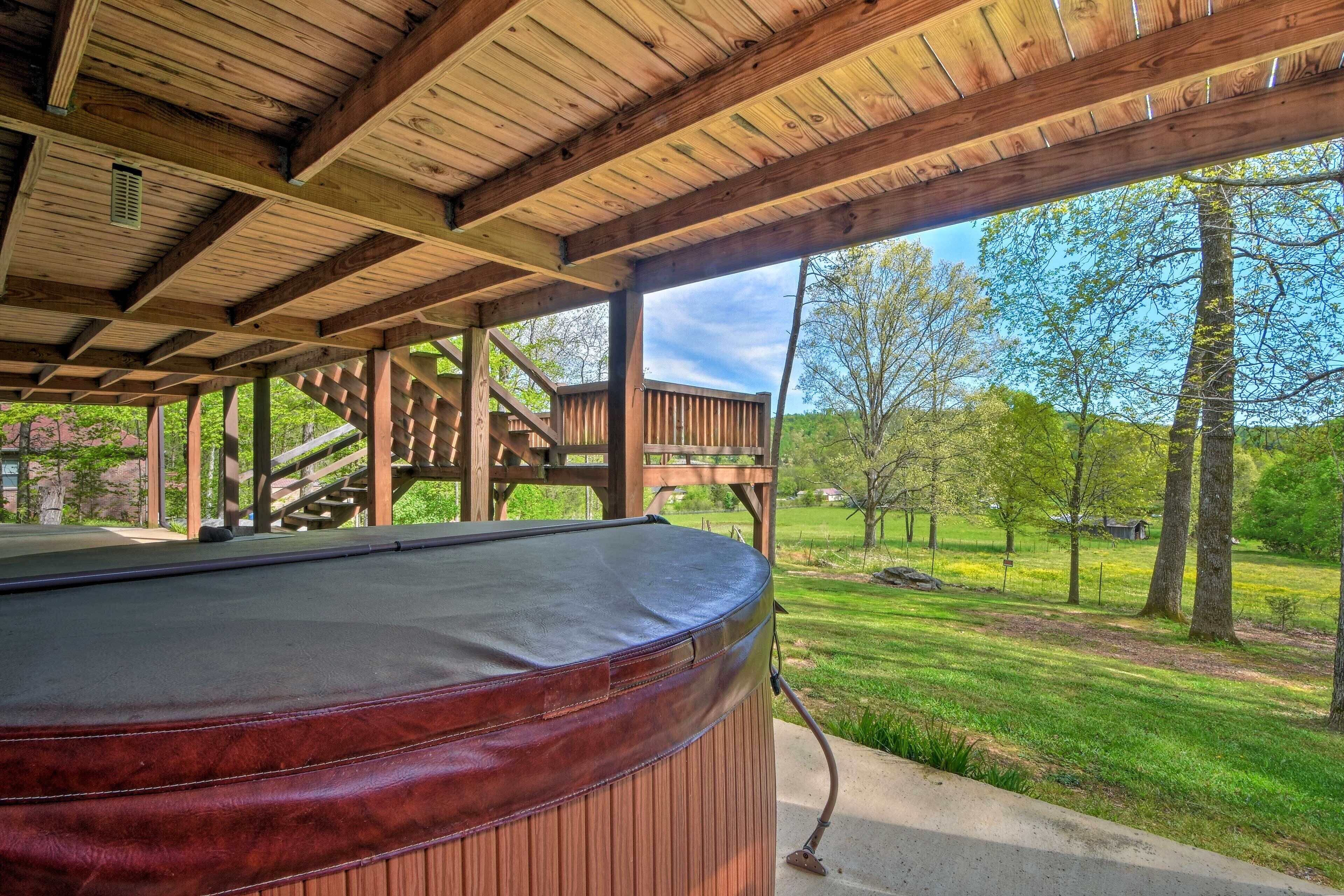 Una terraza de madera con un jacuzzi, rodeada por otra terraza de madera y vistas a un área verde con árboles.