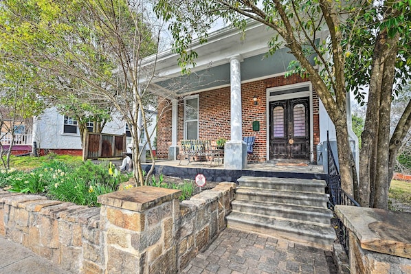 A brick house with a front porch, stone steps, and a garden with yellow flowers.
