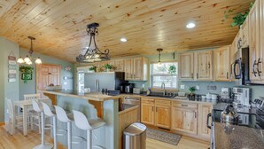 Una cocina con armarios de madera, una isla central con taburetes de bar, electrodomésticos de acero inoxidable y una lámpara colgante.