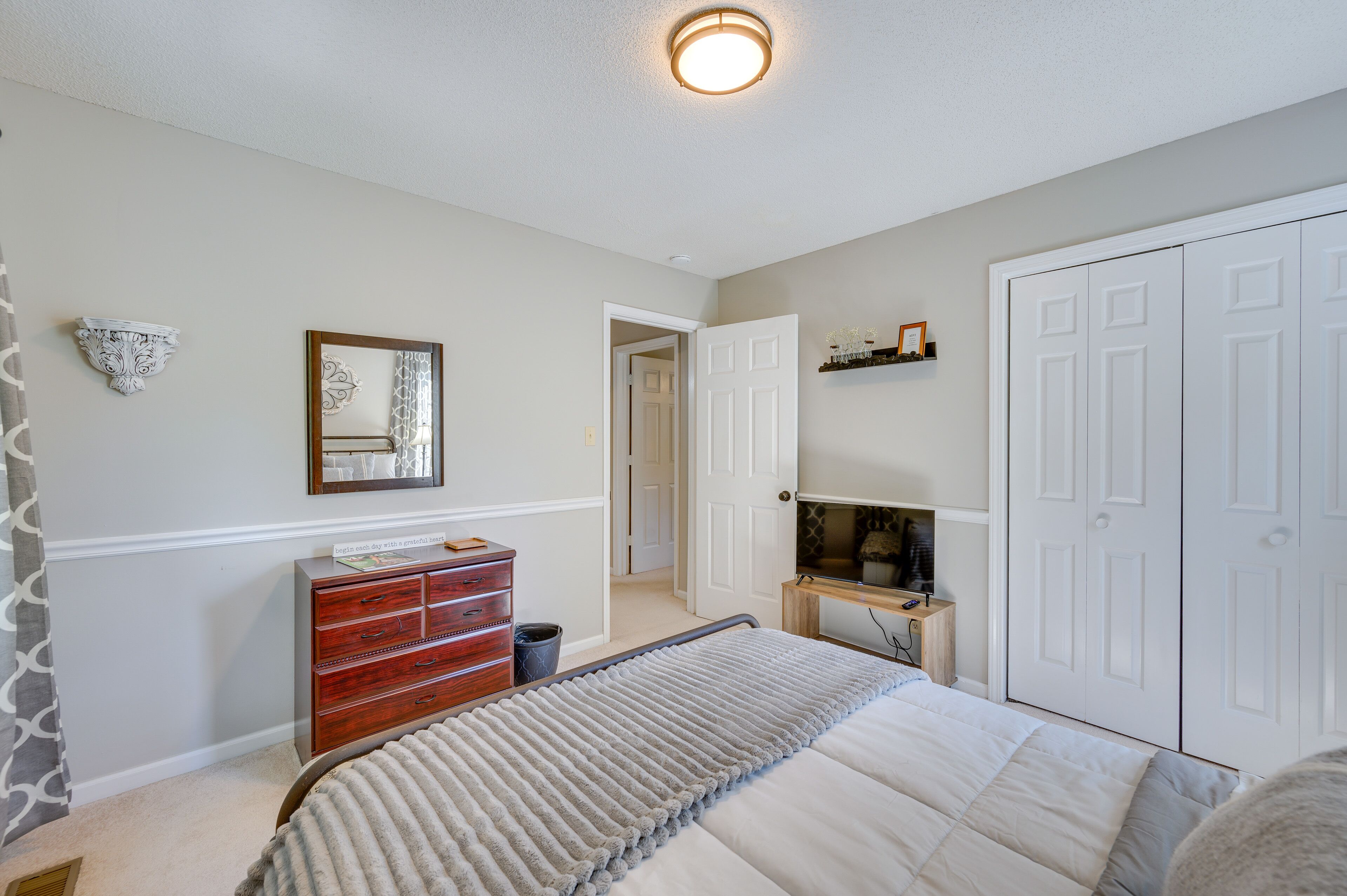 A bedroom with a bed, dresser, TV stand, and wardrobe.