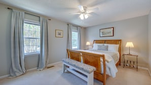 A bedroom with a wooden bed, a bench, two bedside lamps, a ceiling fan, and two windows with curtains. - North Macon Townhome w/ Deck < 8 Mi to Downtown! (Macon)