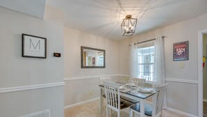 A dining area with a glass table, white chairs, a chandelier, and framed artwork on the walls. - North Macon Townhome w/ Deck < 8 Mi to Downtown! (Macon)