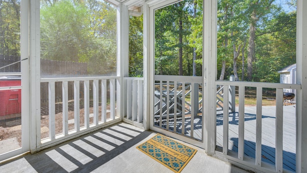 A covered porch with a white railing, a doormat, and a view of a wooded area. - North Macon Townhome w/ Deck < 8 Mi to Downtown! (Macon)