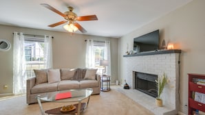A living room with a beige sofa, a glass coffee table, a fireplace, and a television mounted above it. - North Macon Townhome w/ Deck < 8 Mi to Downtown! (Macon)