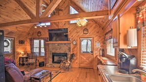 A cozy cabin interior with a stone fireplace, wooden beams, a sofa, a coffee station, and a stone wall.