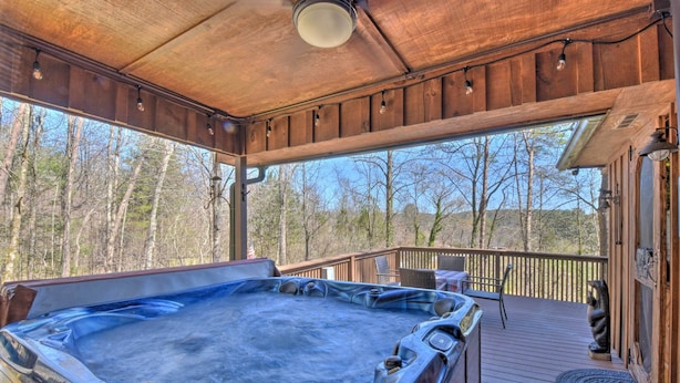 A wooden deck with a hot tub, outdoor seating, and a view of trees.