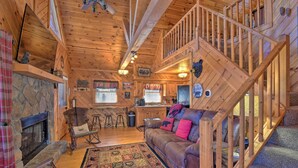 A cozy cabin interior with a wooden staircase, a fireplace, a leather sofa, and a dining area.