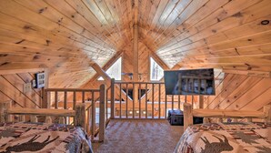 A cozy attic bedroom with wooden beams, a bed, a TV, and a window.