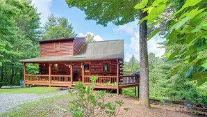 Une cabane en rondins avec un porche, entourée d’arbres et bordée d’une allée de gravier.