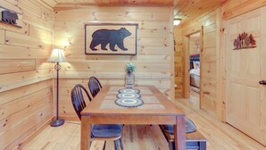 Un intérieur en bois comprenant une table à manger, des chaises, une lampe et la silhouette d’un ours sur le mur.