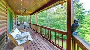 Une terrasse en bois avec un fauteuil suspendu et une statue de hibou.