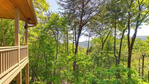 A wooden deck overlooking a forested area with trees and a distant view of hills. - 2 Queen Suites, Trail Access, Mtn View, Fire Table (Blue Ridge)
