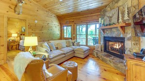 A cozy cabin interior with a fireplace, wooden walls, a sofa, and a ceiling fan. - 2 Queen Suites, Trail Access, Mtn View, Fire Table (Blue Ridge)
