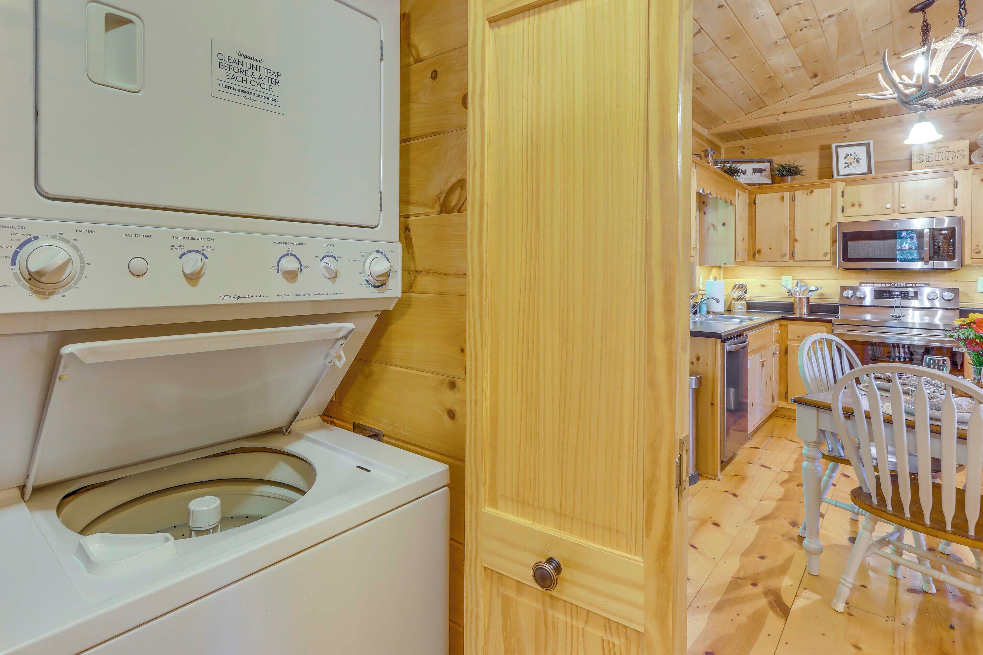 A laundry area with a front-loading washer and dryer, wooden interior, and a kitchen with a microwave and sink.
