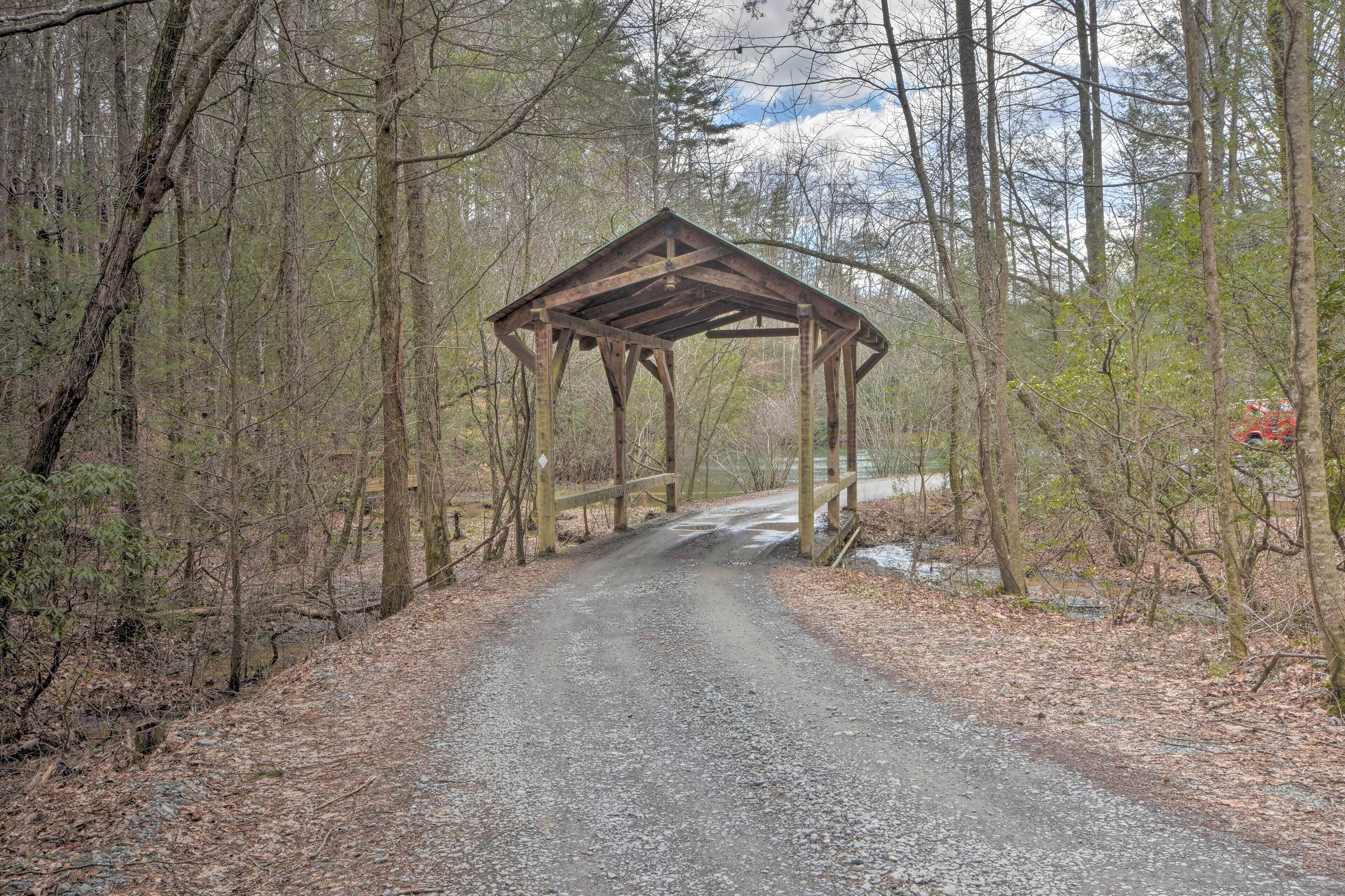 A wooden gazebo structure on a gravel path surrounded by trees.